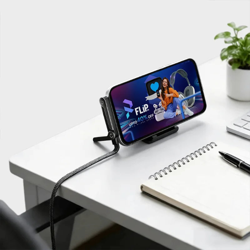 Smartphone on a stand displaying an app interface on a white desk with a plant and notebook.